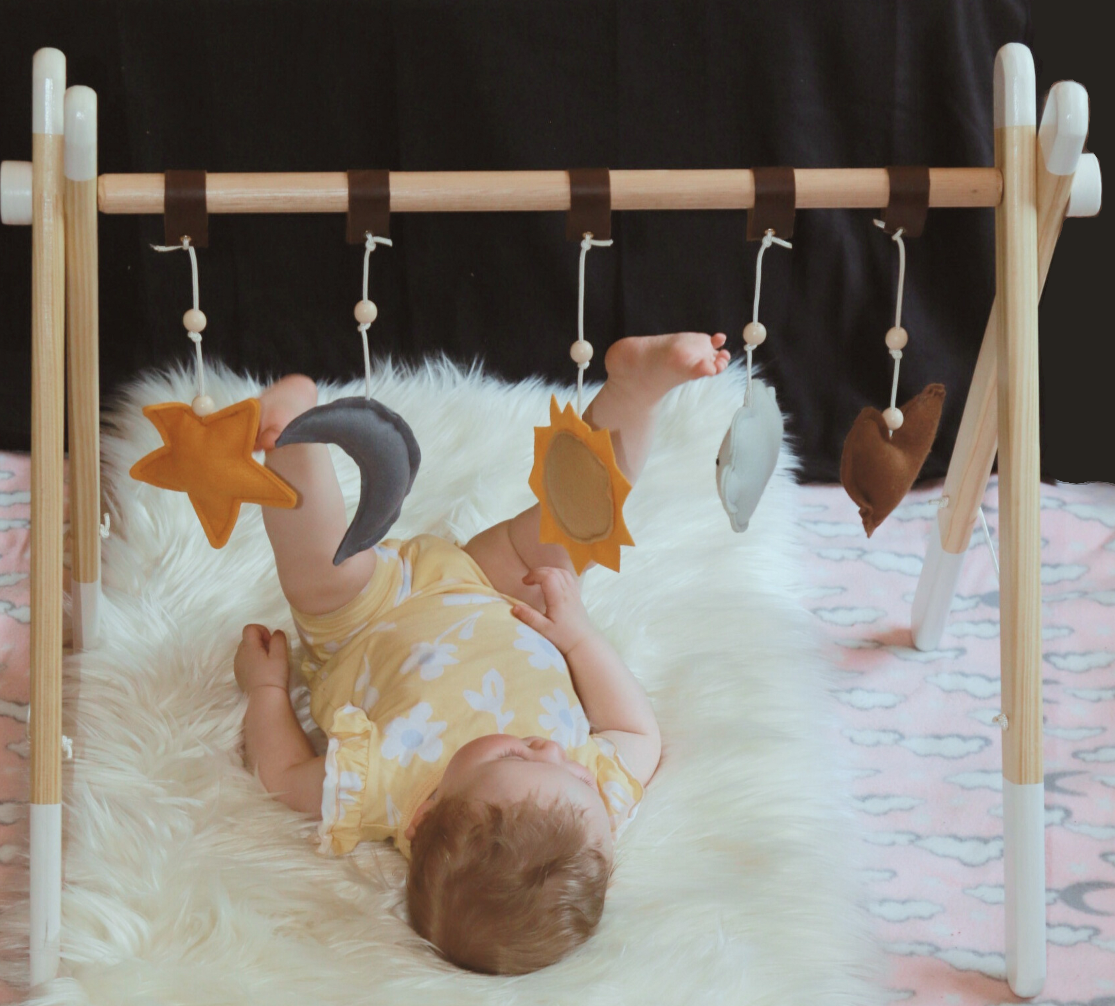 Baby lying on a fluffy blanket with a wooden baby gym and hanging dangle toys. Two Eddyphants, Local, South Africa